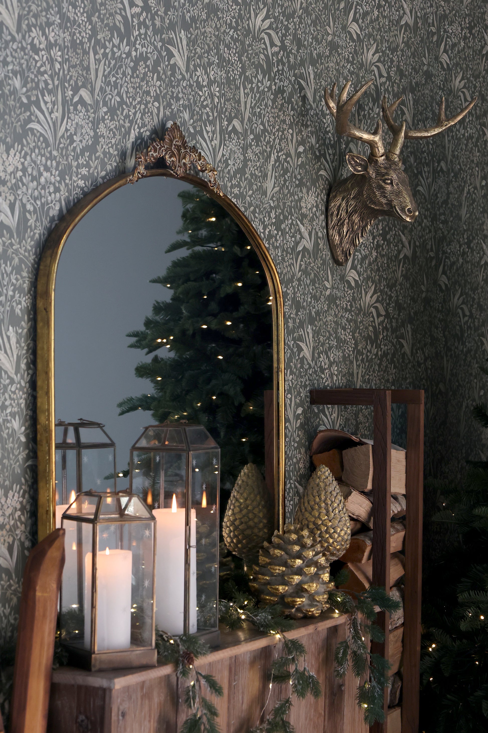 Decorative mirror with ornate frame on a wall with a deer head mount, candle lanterns, and decorative items.