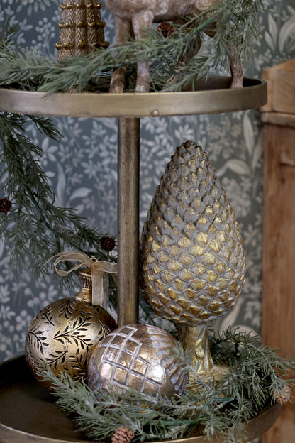 Decorative tiered stand with gold ornaments and greenery against a patterned wall.