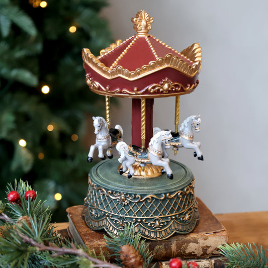 Decorative carousel with horses on a stand in front of a Christmas tree.