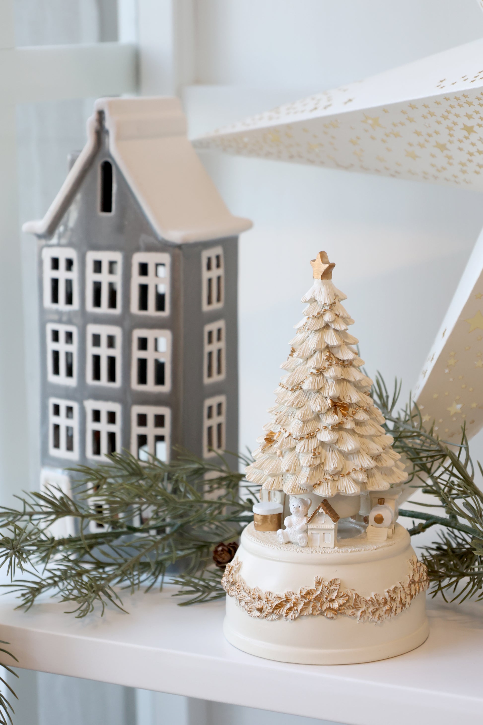 Decorative Christmas tree with a small house and greenery on a shelf.