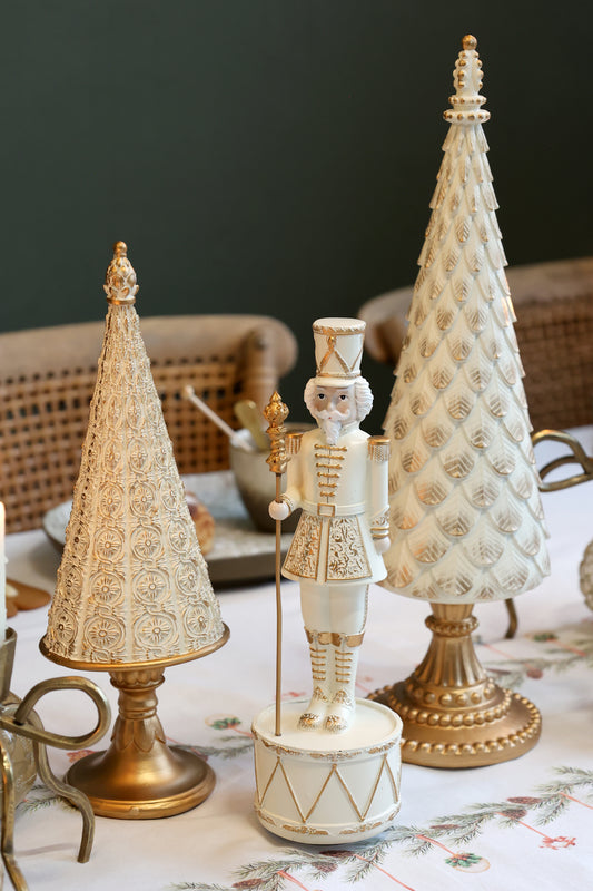 Decorative Christmas scene with a nutcracker and two gold and white trees on a table.