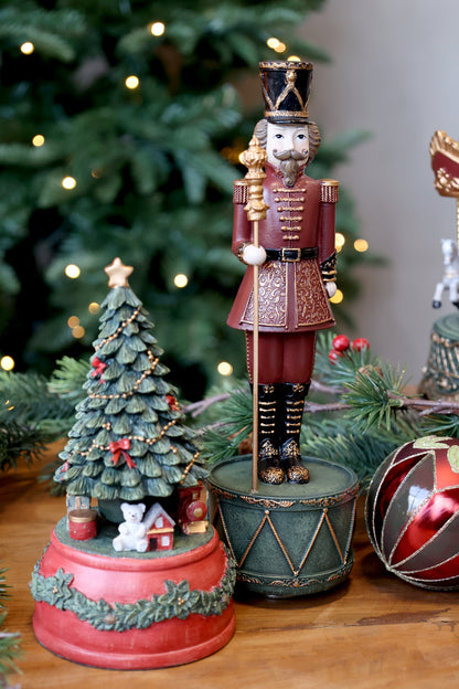 Decorative nutcracker and Christmas tree figurines on a wooden surface with a blurred Christmas tree in the background.