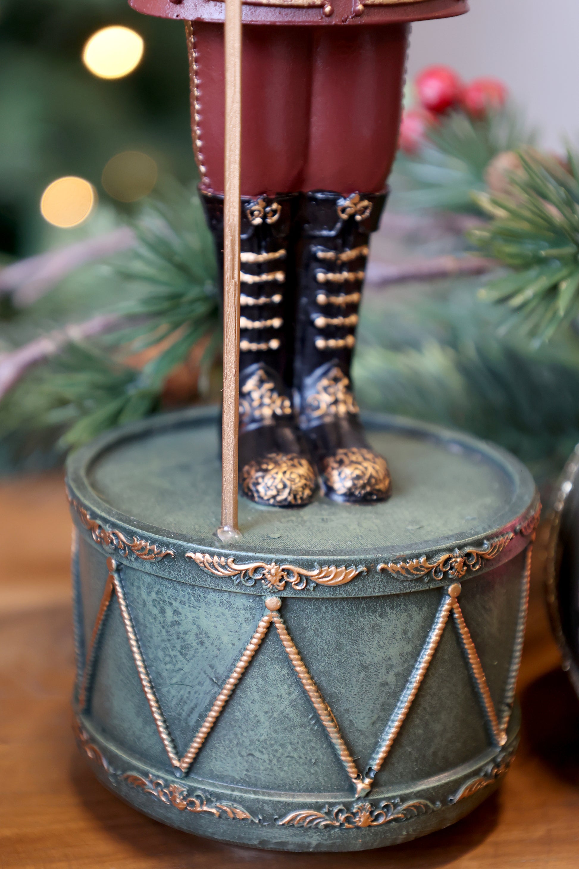 Decorative figurine of a person in military uniform standing on a drum with Christmas decorations in the background.