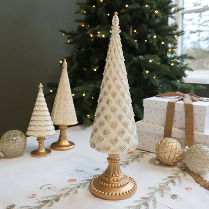 Decorative Christmas trees with gold bases on a table in front of a decorated tree.