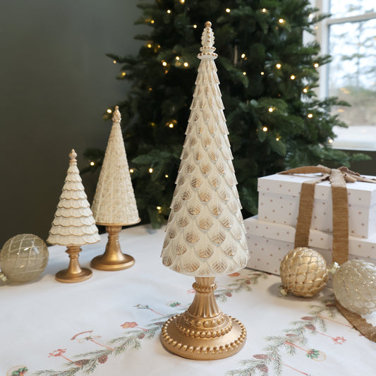 Decorative Christmas trees with gold bases on a table in front of a decorated tree.
