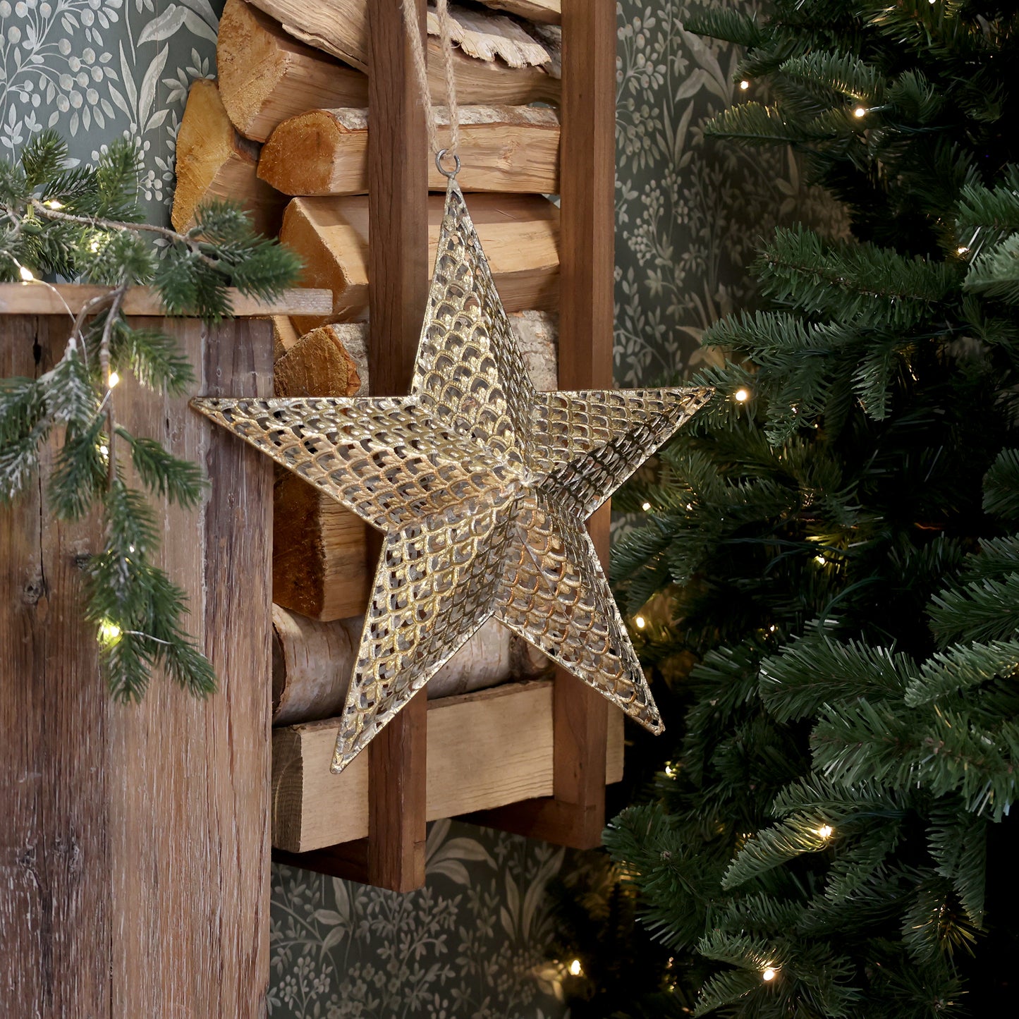 Decorative star hanging on a wooden wall with Christmas tree and lights in the background