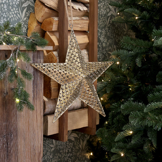 Decorative star hanging on a wooden wall with Christmas tree and lights in the background