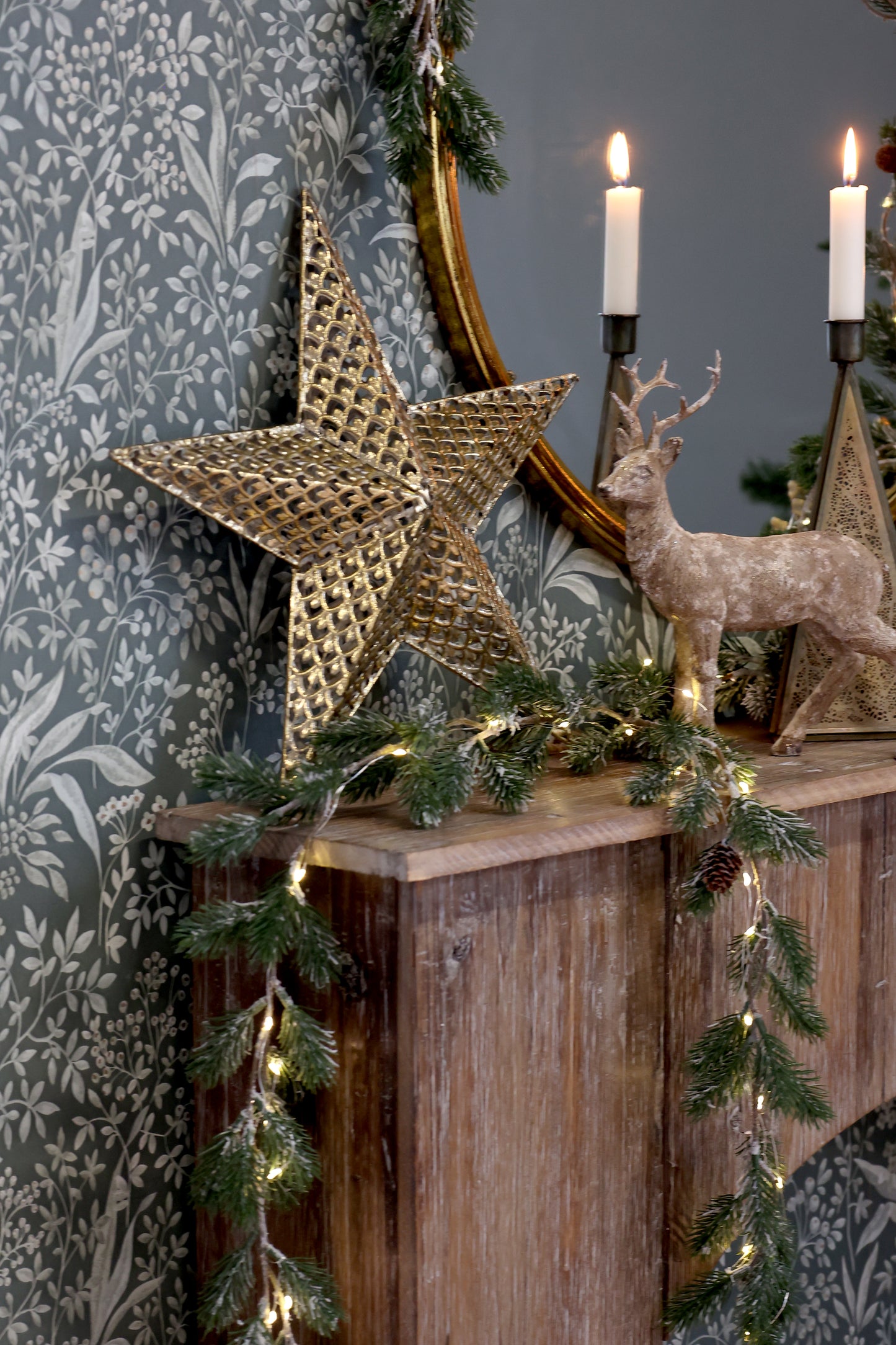 Decorative mantel with Christmas decorations including a star, deer, and candles against a patterned wall.