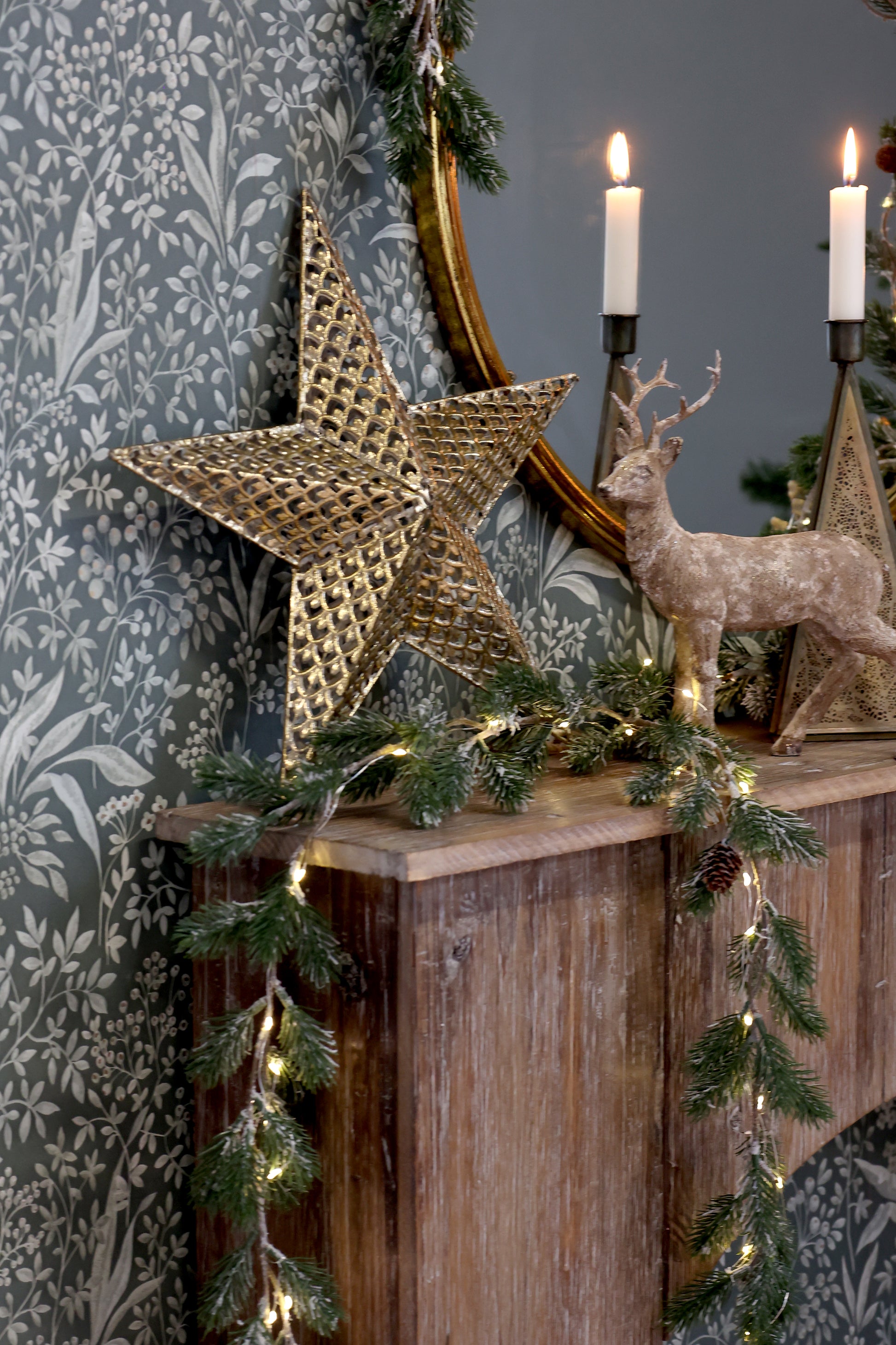 Decorative mantel with Christmas decorations including a star, deer, and candles against a patterned wall.