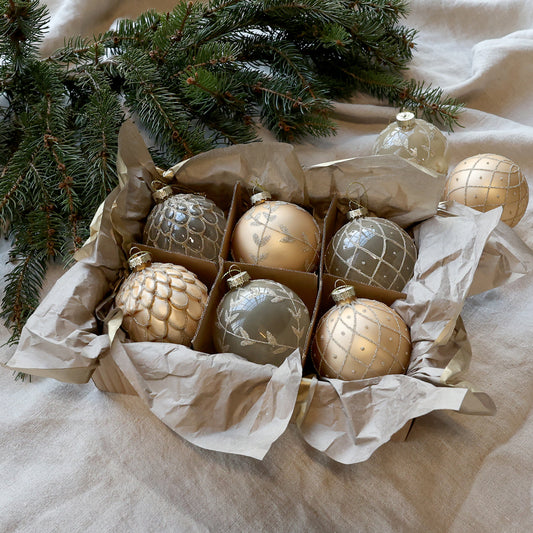 Box of gold and silver Christmas ornaments on a beige fabric background with a tree branch.