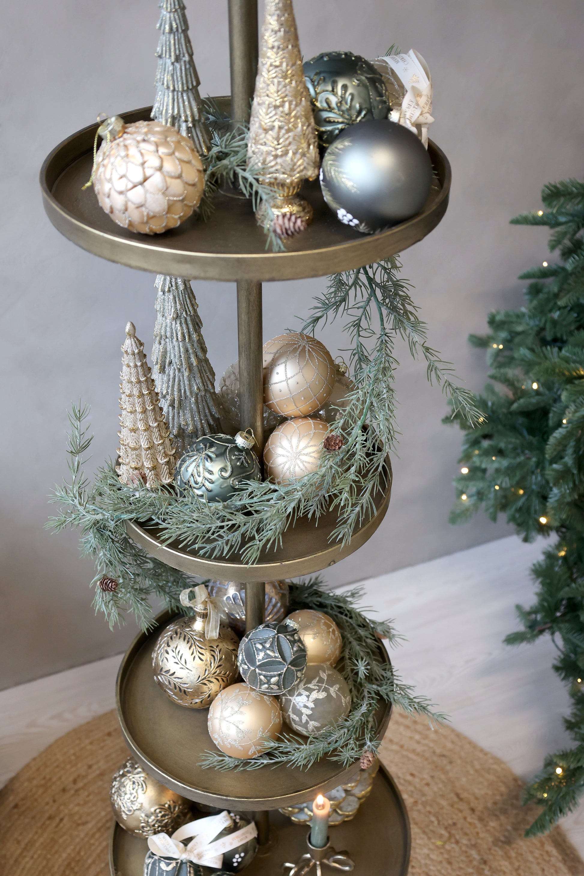 Decorative tiered stand with Christmas ornaments and greenery against a neutral background