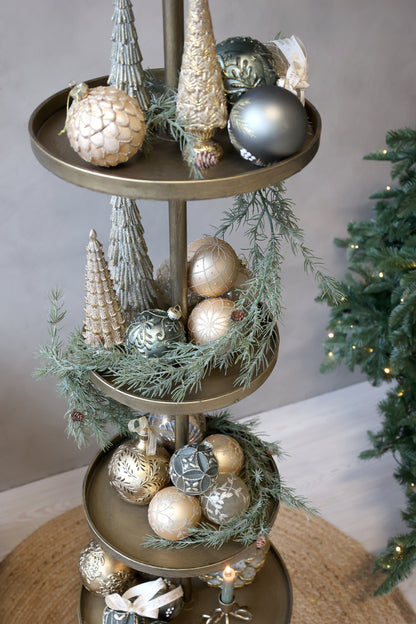 Decorative tiered stand with Christmas ornaments and greenery against a neutral background