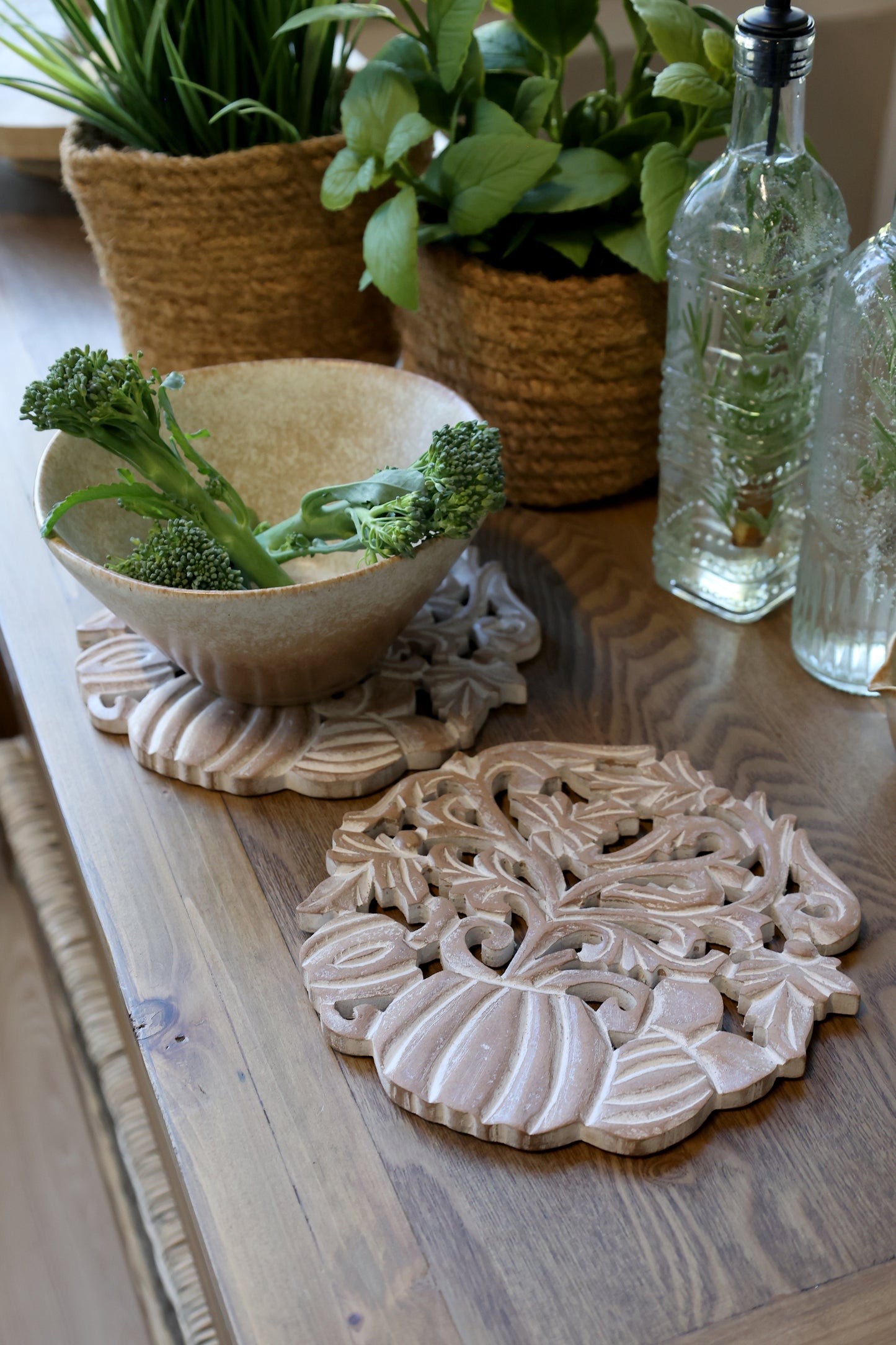 Decorative ceramic trivets on a wooden surface with plants and bottles in the background