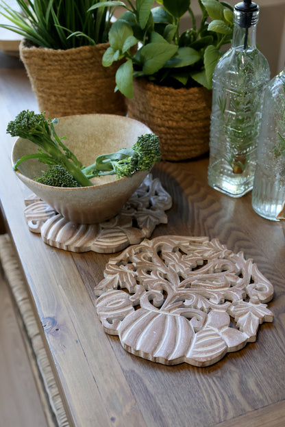 Decorative ceramic trivets on a wooden surface with plants and bottles in the background