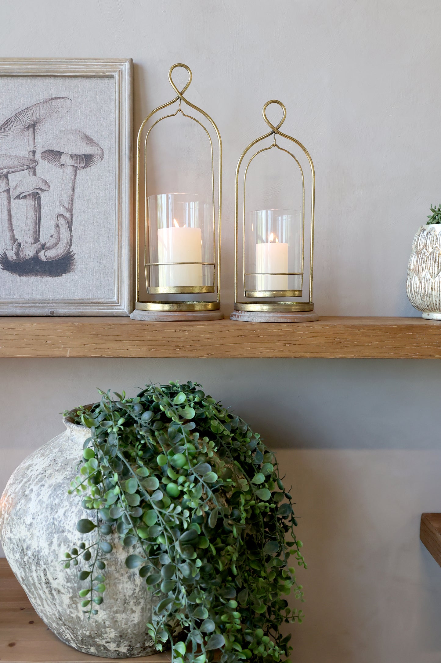 Decorative shelf with gold candle holders, candles, and a framed picture on a neutral wall.