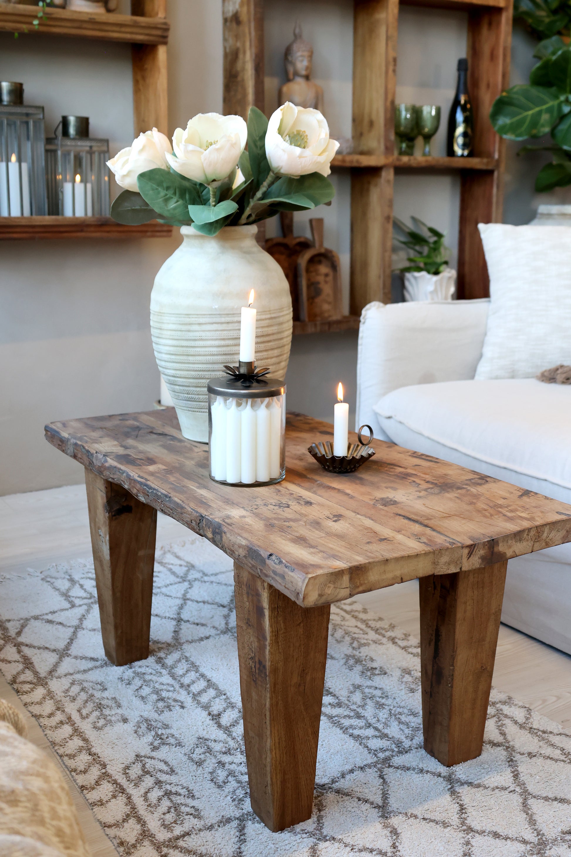 Living room with a wooden coffee table, white vase with flowers, and candles.