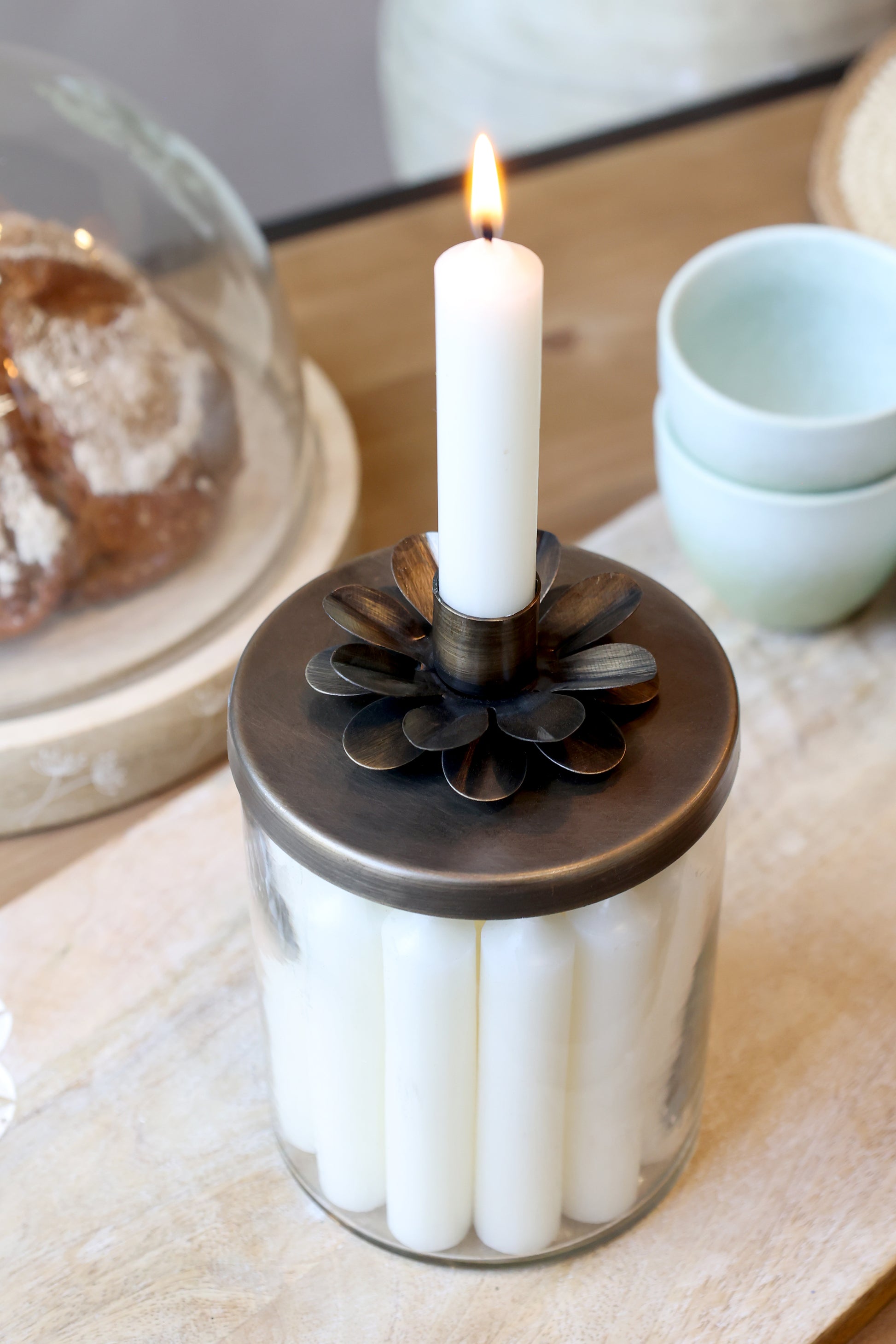 Candle holder with a lit candle on a table with pastries and cups in the background