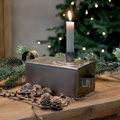 Decorative candle holder with a lit candle on a wooden surface with Christmas decorations.
