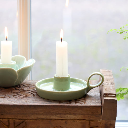 Candle in a green ceramic holder on a wooden surface with a blurred background