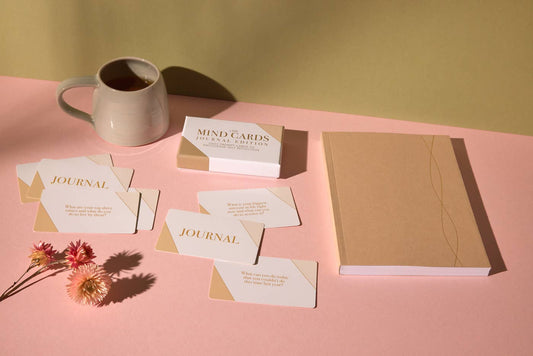 Journals, cards, and a mug on a pink surface with a yellow background