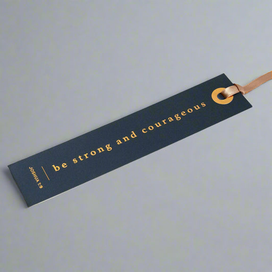 Open book with a blue bookmark featuring 'be strong and courageous' text.